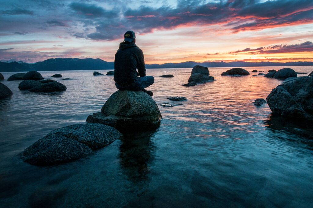 夕暮れの水辺で石の上に座る人